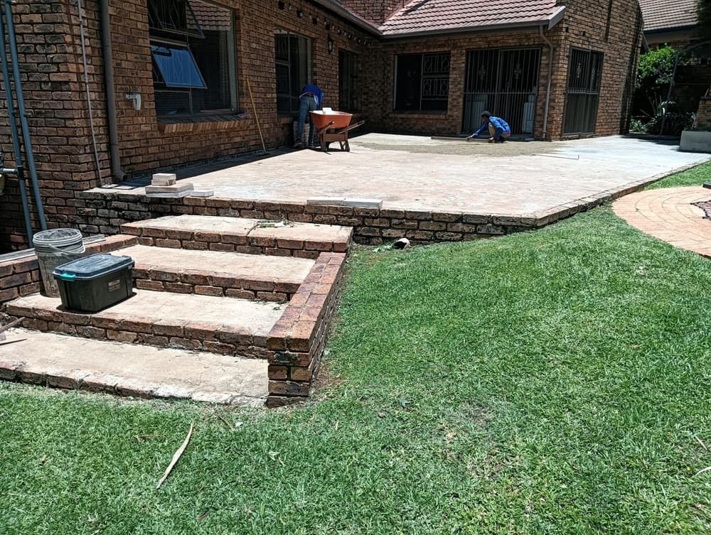 two workers preparing a raised patio at a face brick house